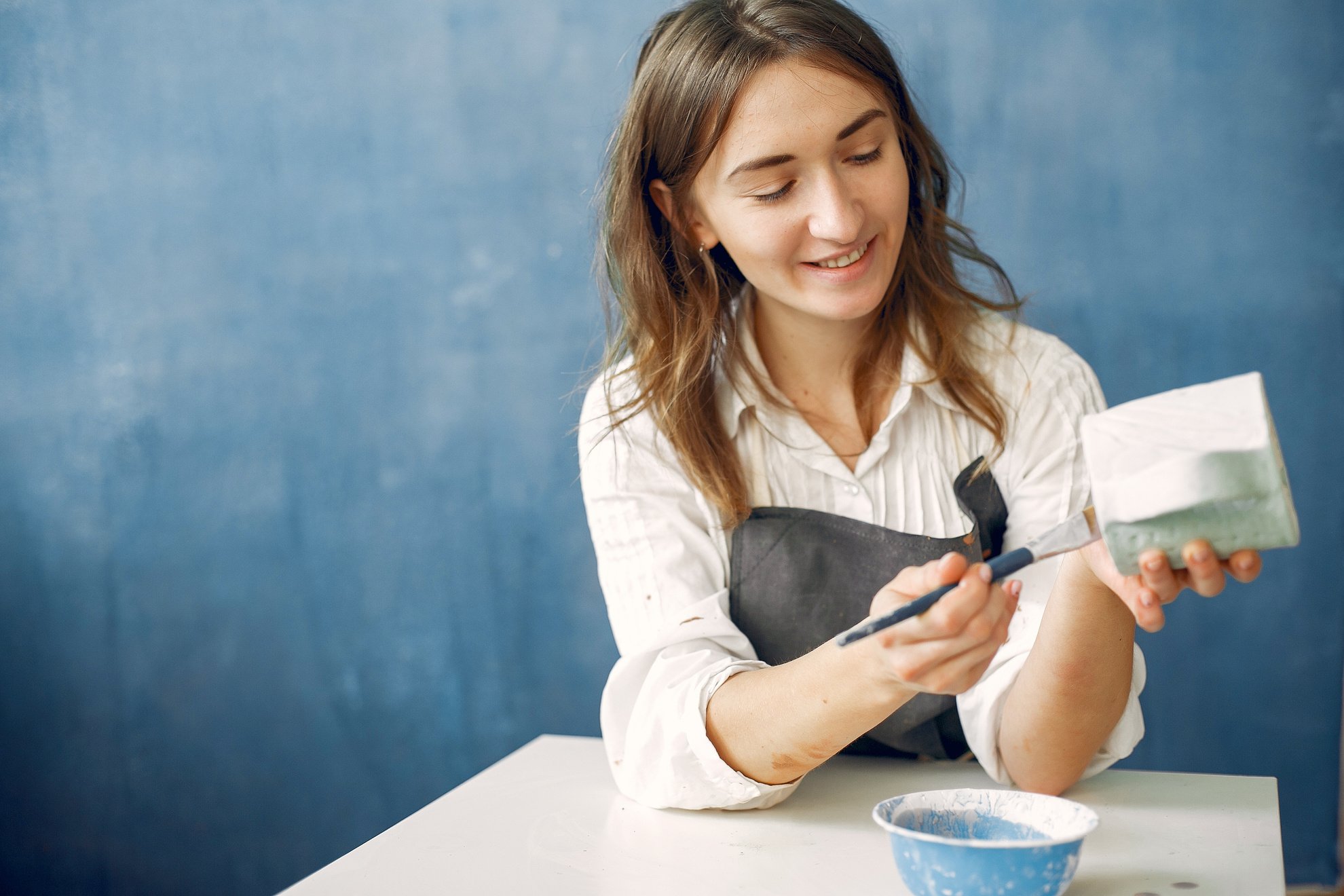 Cheerful craftswoman painting ceramic cup with paintbrush